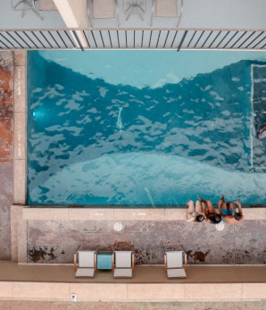 An aerial view of a swimming pool with sun loungers on the side; three people stand by the pool
